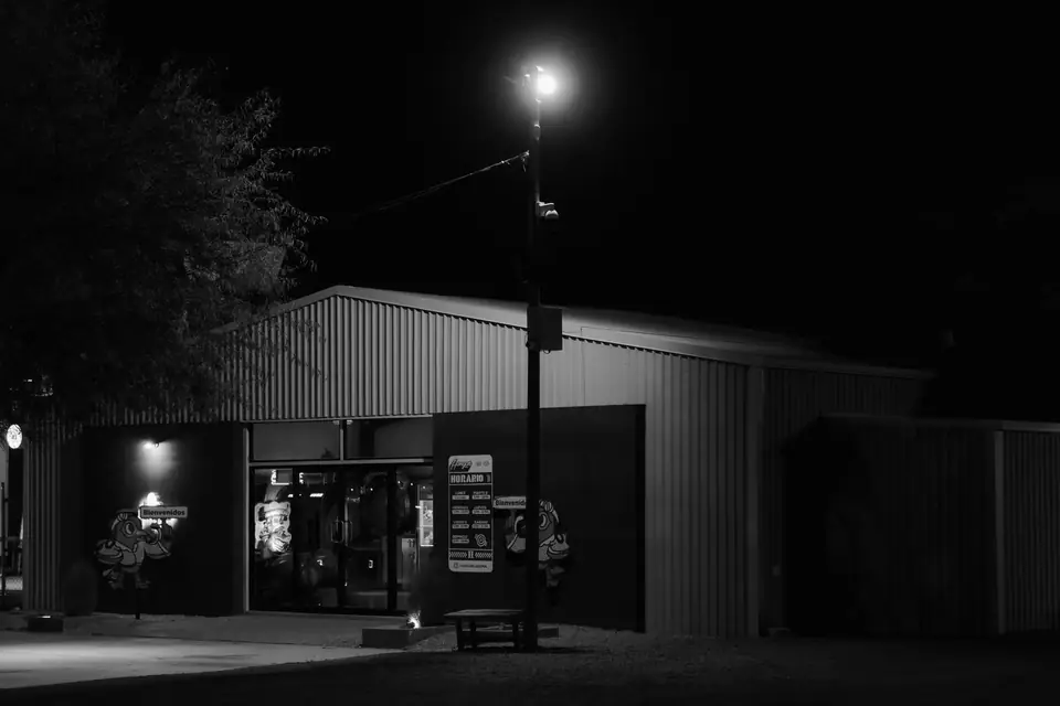 A metal-sided building with an open, lit doorway stands beneath a single streetlamp at night.