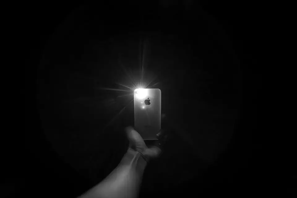 A hand holds up a smartphone in a dark room, its camera light shining brightly.