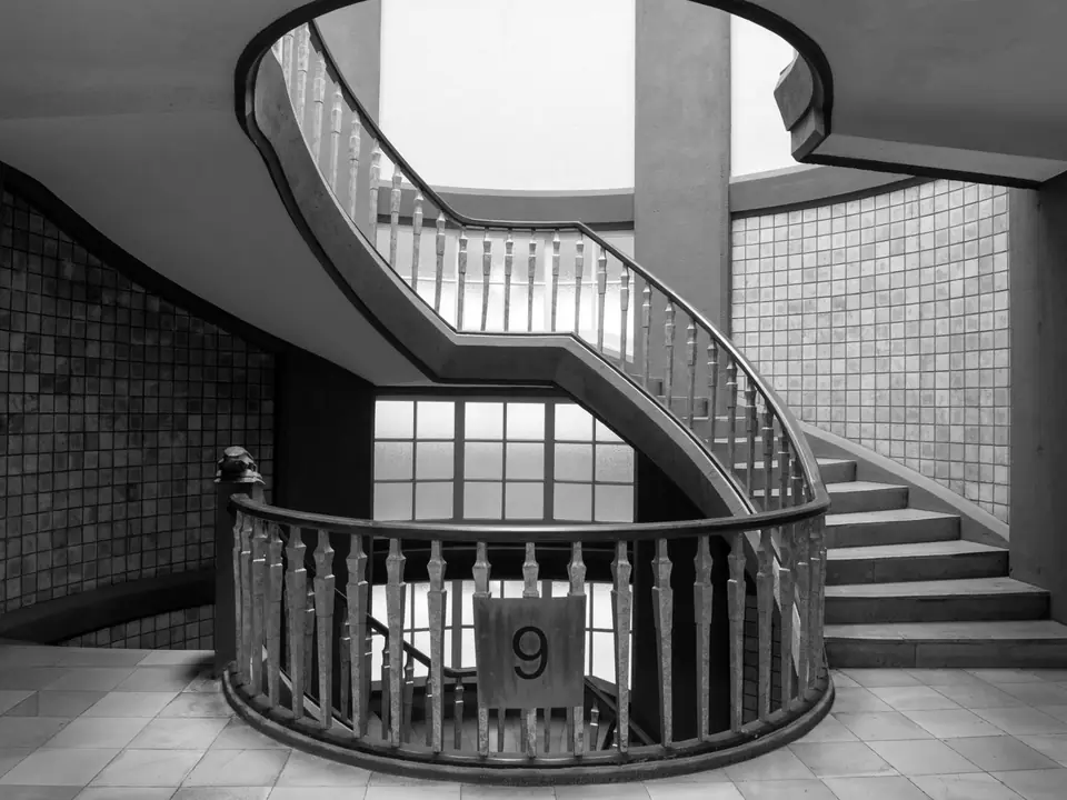 A curved staircase with wooden railings spirals up around a tiled wall, with a number 9 on the landing.