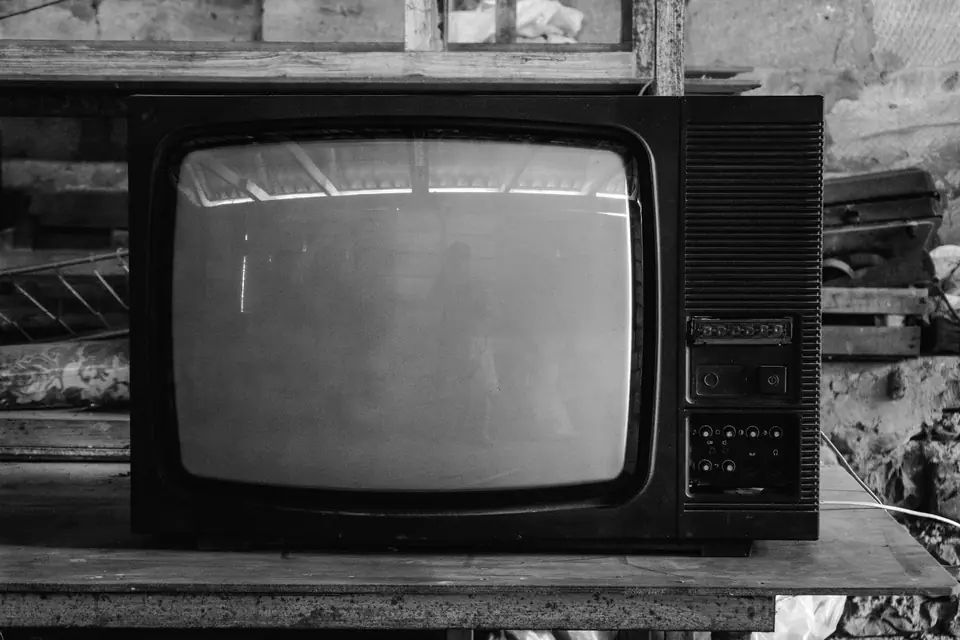 A large old television with a blank screen sits on a wooden table in a cluttered workshop.
