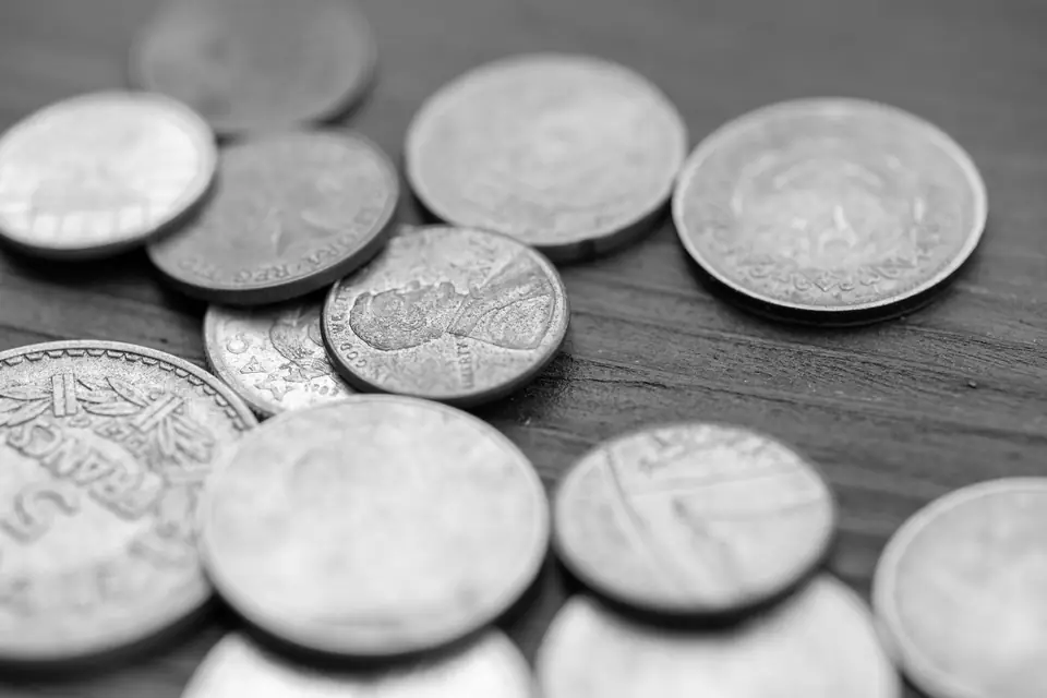 A close view of a pile of assorted coins scattered across a wooden table.
