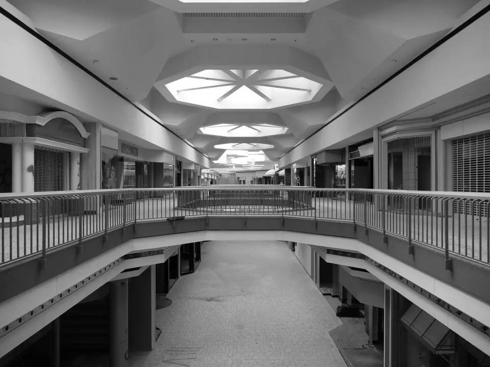 An empty two-level shopping mall with railings and star-shaped skylights in the ceiling.
