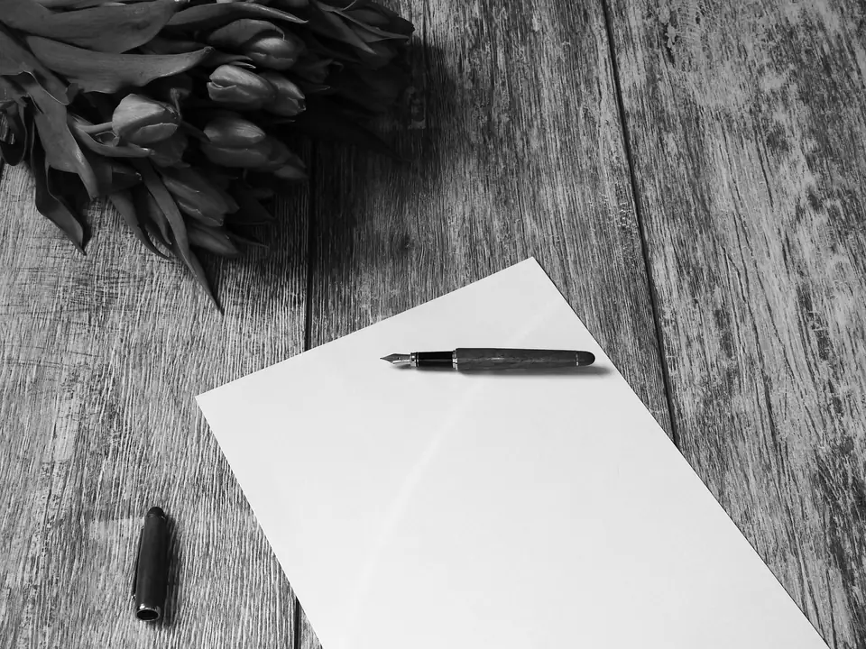A fountain pen and its cap lie on a blank sheet of paper on wooden boards beside tulips.