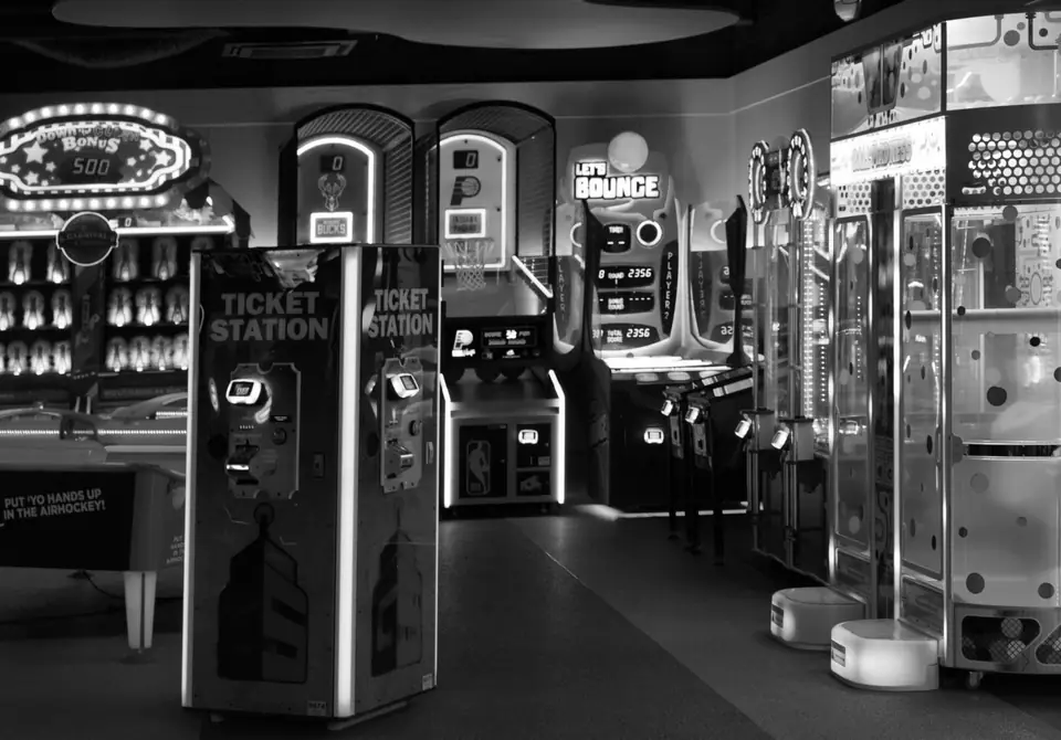 A brightly lit modern arcade is filled with ticket stations, claw machines and basketball games.