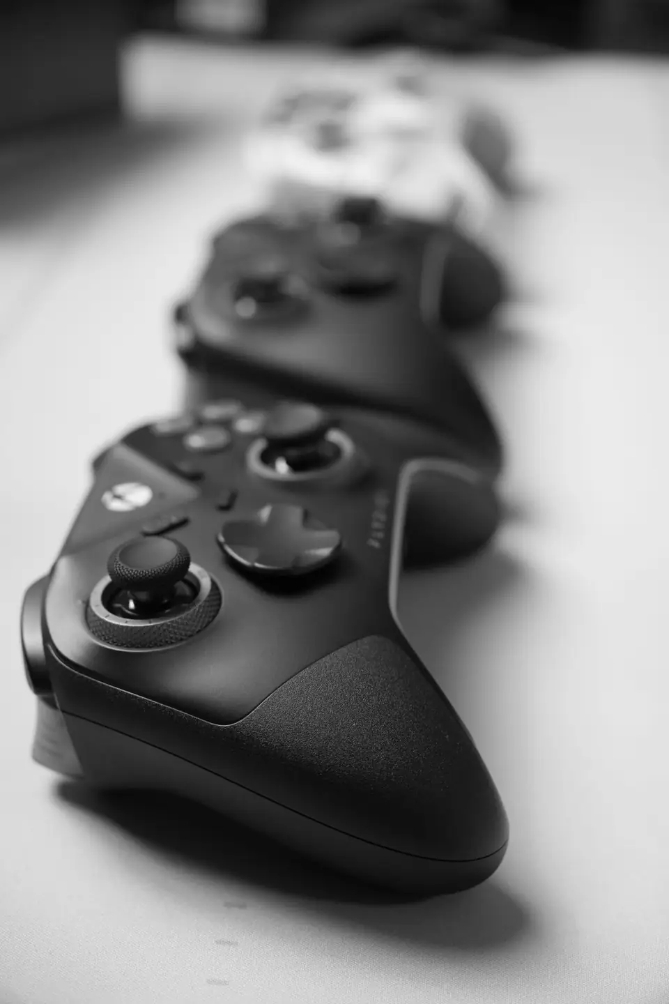 A row of dark game controllers with thumbsticks recedes out of focus along a table.