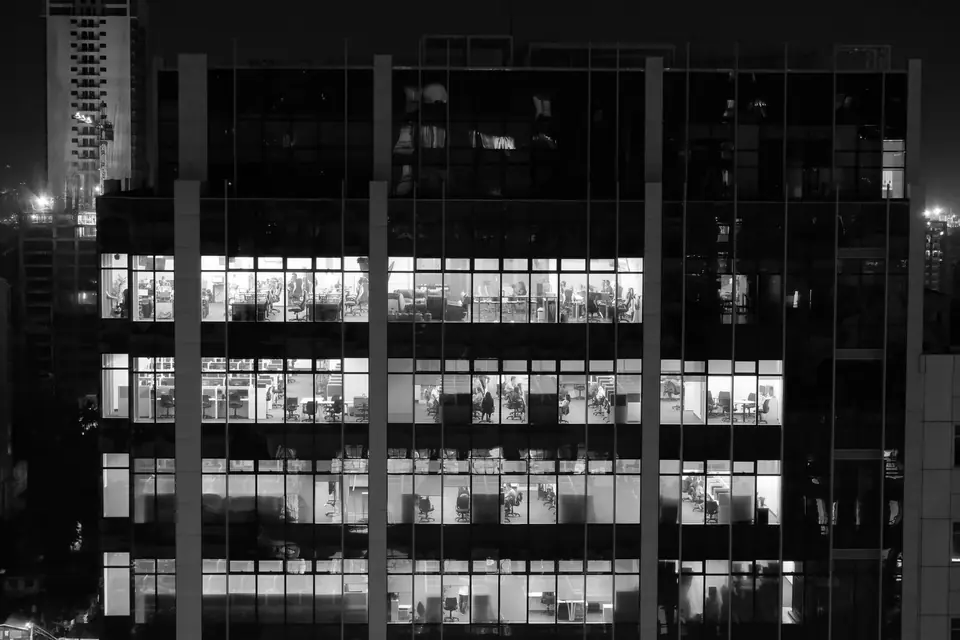An office building at night with several brightly lit floors behind a glass facade.