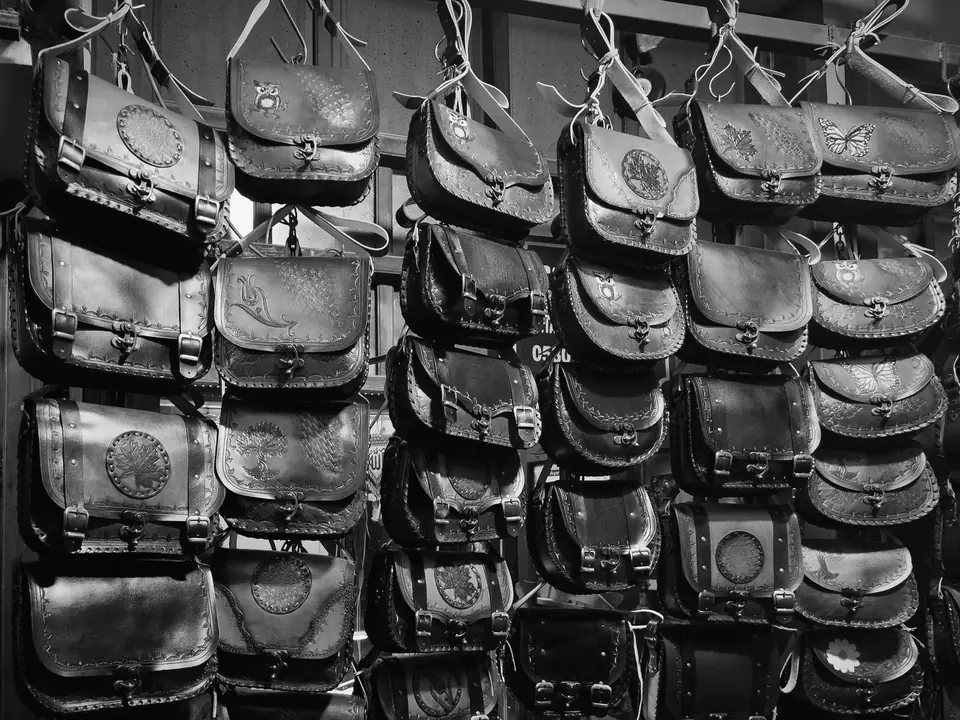 Dozens of leather satchels with embossed designs hang in tight rows on a market stall wall.