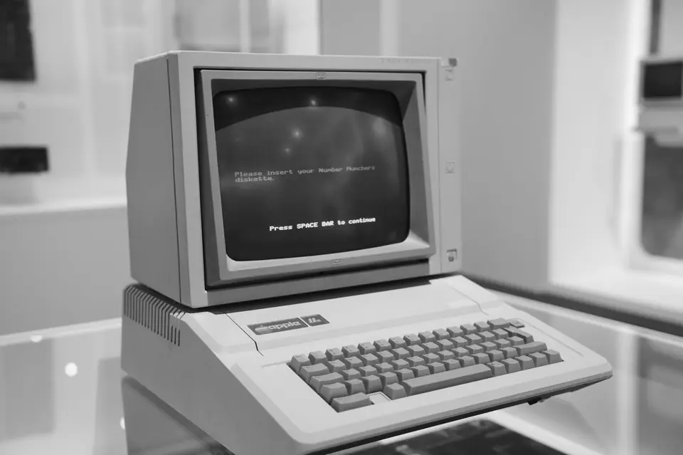 A vintage beige computer on a display stand shows text on its green-tinted screen.