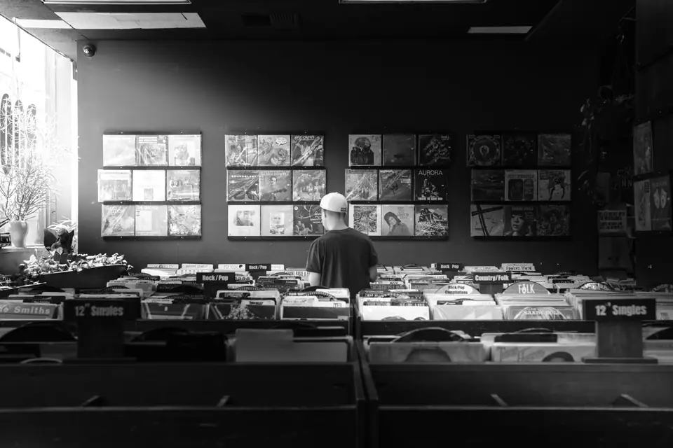 A man in a cap browses long rows of record bins in a store with album covers on the wall.