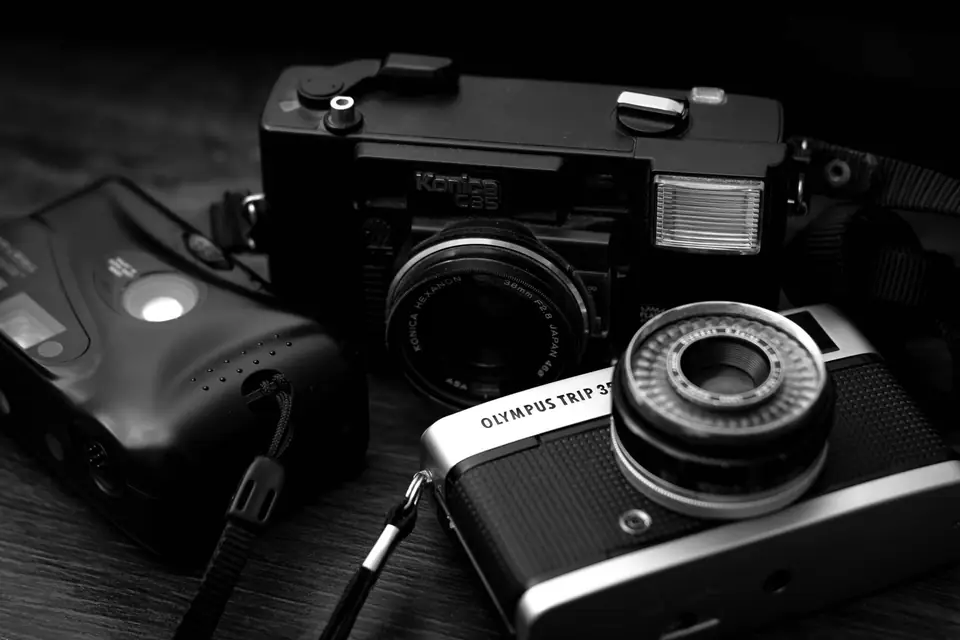 Several vintage compact film cameras, including an Olympus Trip 35, lie together on a dark wooden surface.