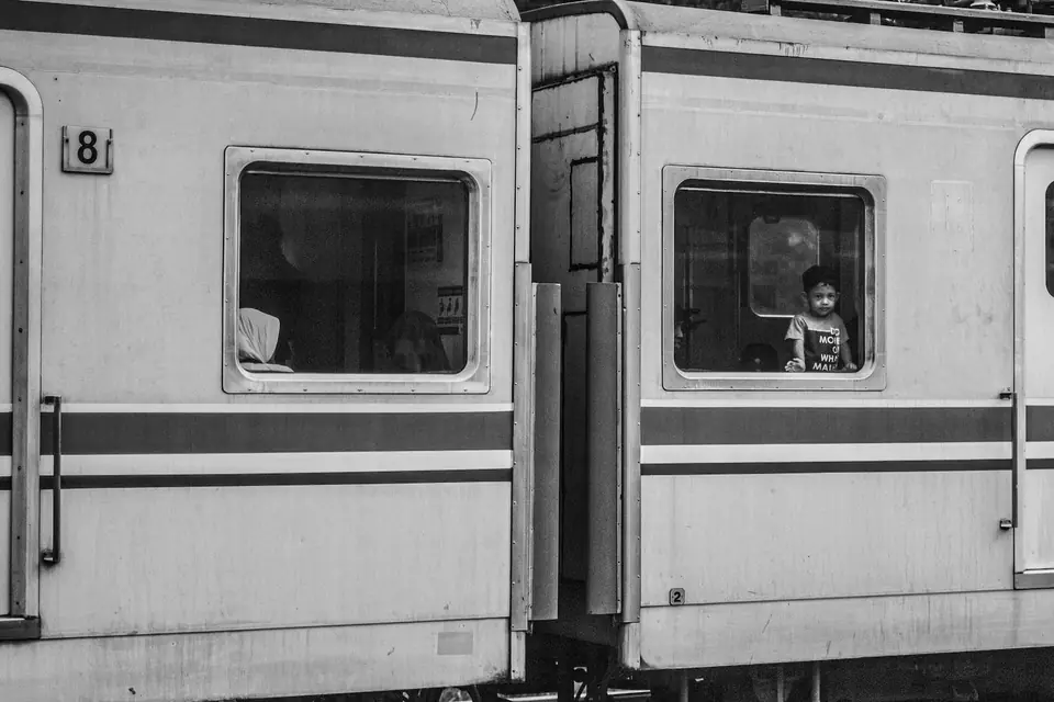 The side of a passenger train with two windows, a young child looking out of one.