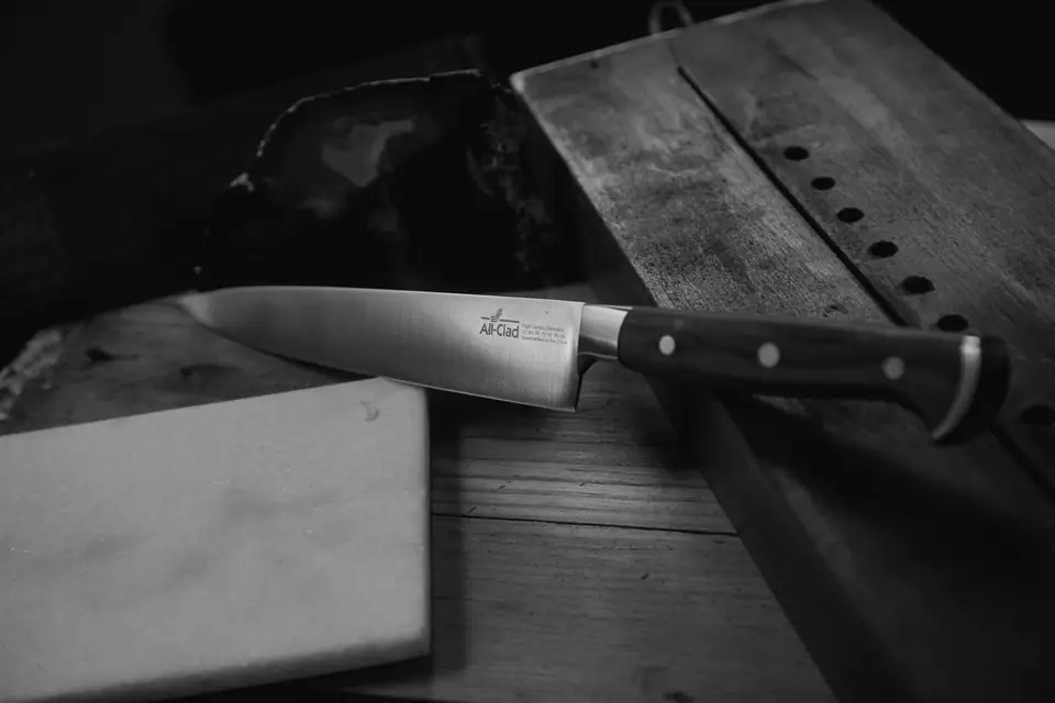 A chef’s knife with a riveted dark handle lies across a wooden cutting board beside a knife block.