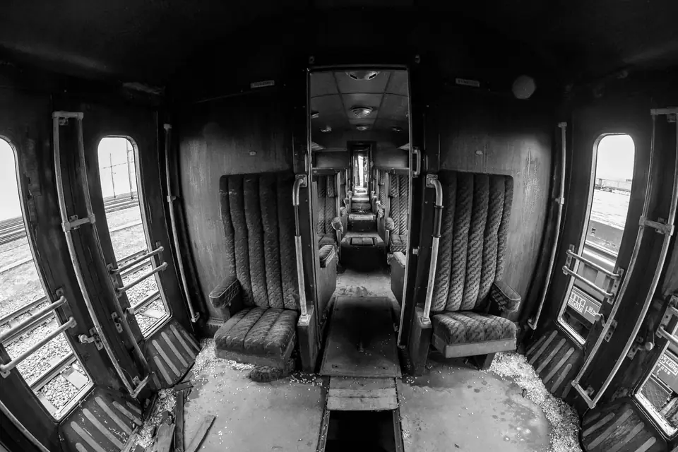 The worn interior of an old, empty train carriage with padded seats and small windows.