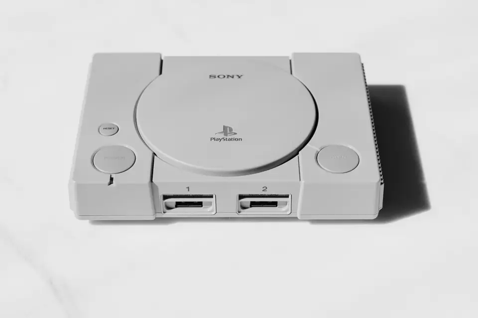 A gray video game console with a round disc lid and two front ports sits on white.