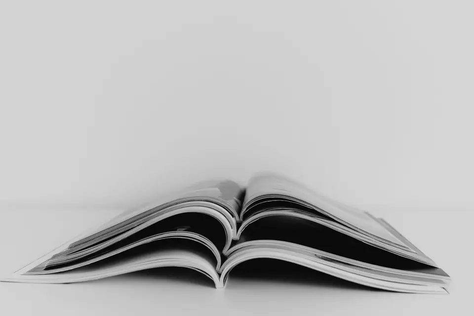 An open magazine lies face down and splayed on a plain white surface against a white background.