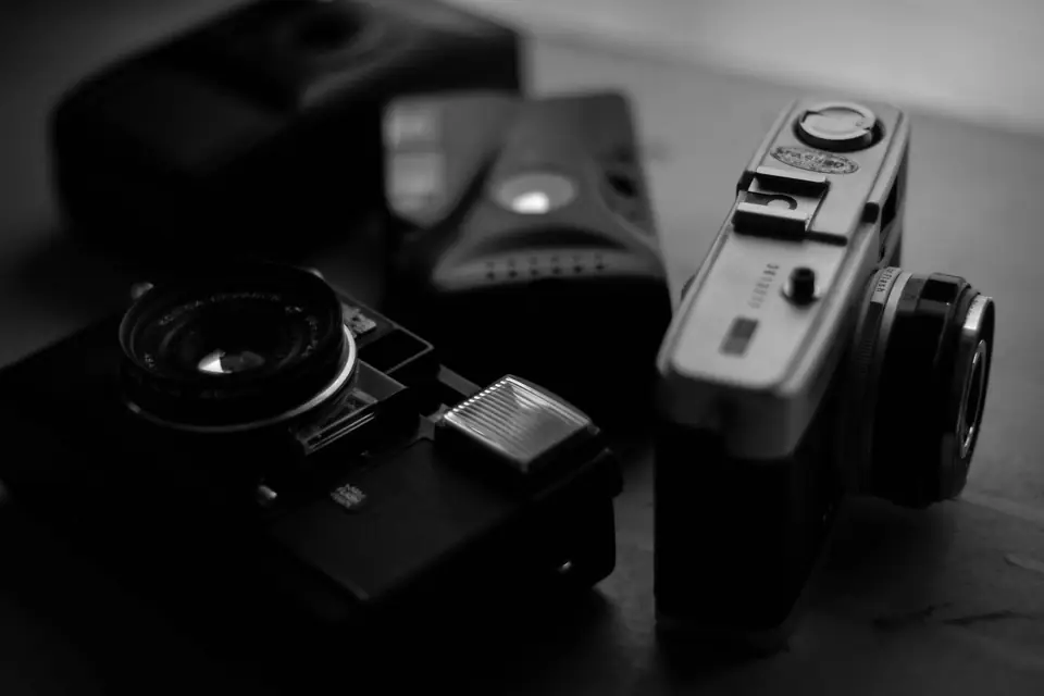 A group of old film cameras with round lenses and flash units sits on a table in soft light.