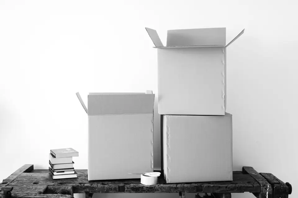 Two open cardboard boxes, a roll of tape and a small stack of books sit on an old wooden workbench.
