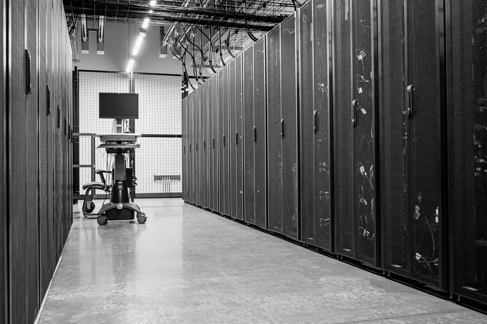 A long, clean corridor lined with tall black server cabinets, with a monitor cart at the far end.