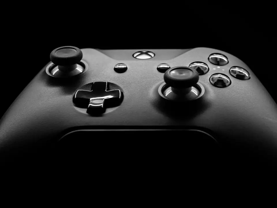 A dark game controller with two thumbsticks, a cross pad and buttons is lit against black.