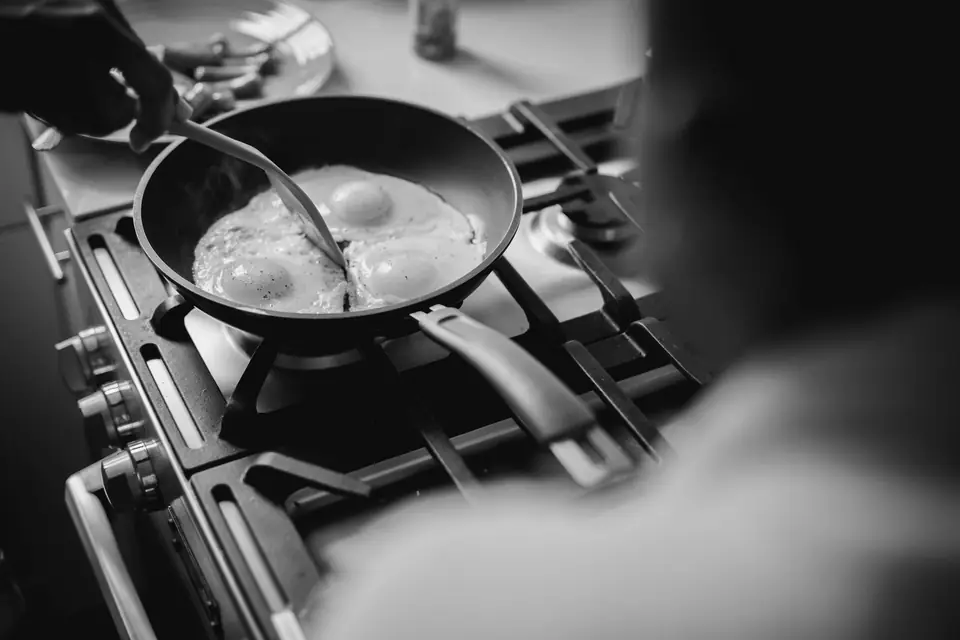 A cook moves a spatula through two fried eggs in a skillet on a gas stove.