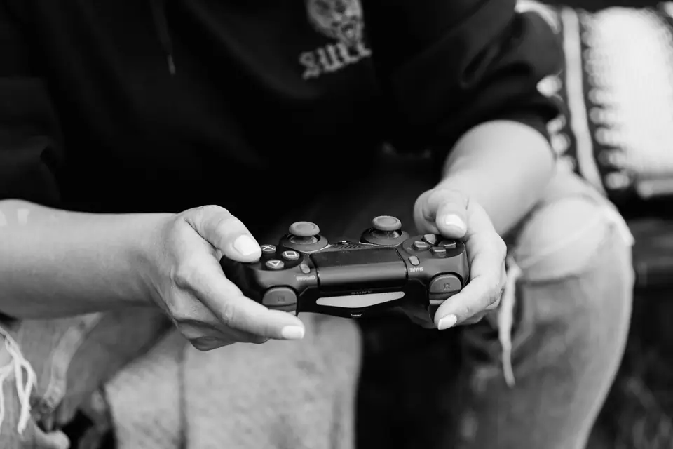 A seated person in jeans holds a black game controller with both hands.
