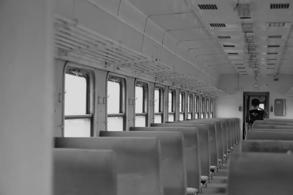 A long train carriage with rows of empty seats and a single passenger standing at the far door.