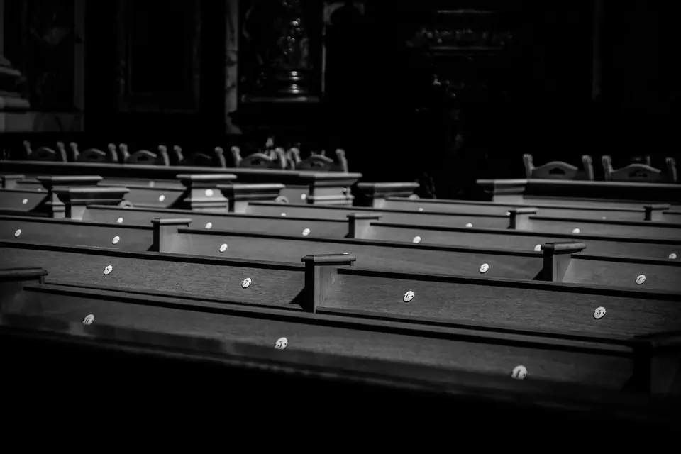 Rows of dark wooden pews fill a dim church interior.