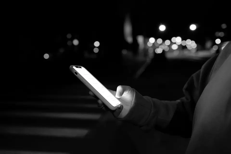 A hand holds a lit smartphone at night, with blurred street lights in the background.