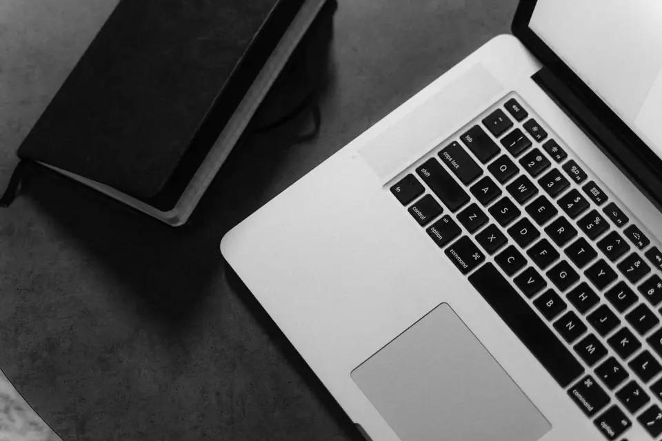 An open laptop keyboard and a closed black notebook sit on a dark desk, seen from above.