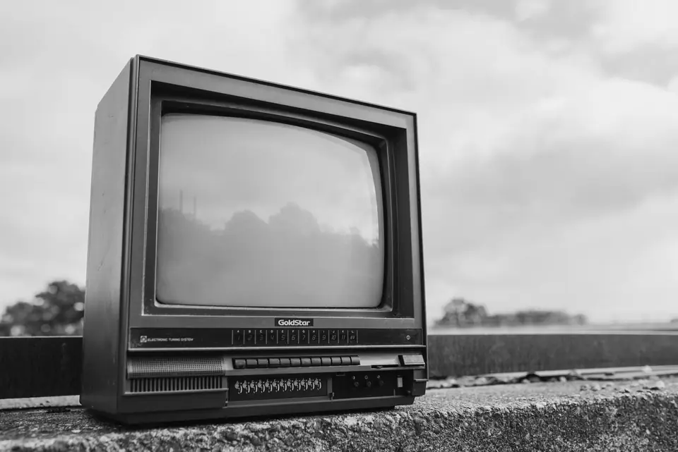 An old television set with a wood-grain cabinet and control panel sits on a concrete ledge outdoors.