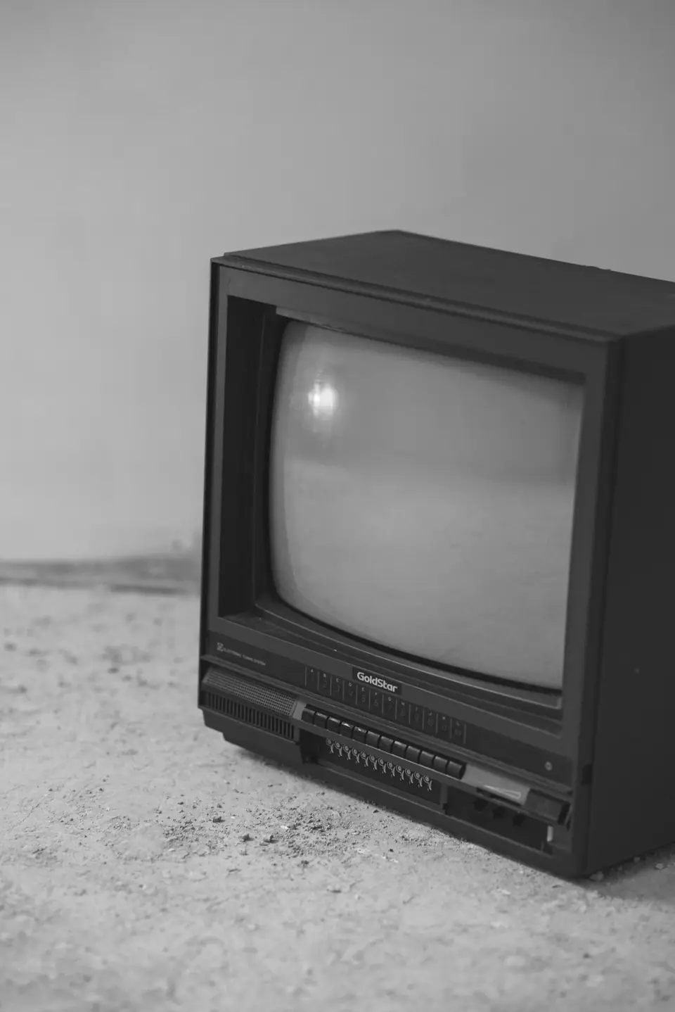 A dark tube television with a curved glass screen sits on a concrete floor.