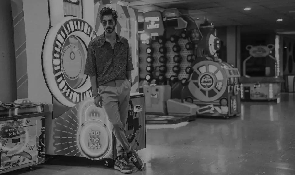 A man in sunglasses leans against an arcade machine in a large amusement hall.