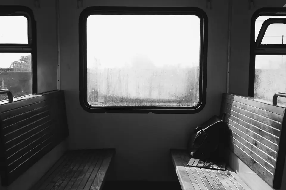 Two wooden benches face each other under a train window, with a bag resting on one seat.
