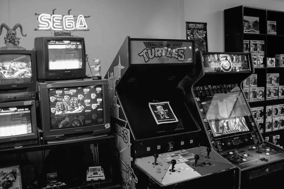 A retro game shop holds arcade cabinets, stacked CRT televisions and shelves of boxed games under a neon sign.