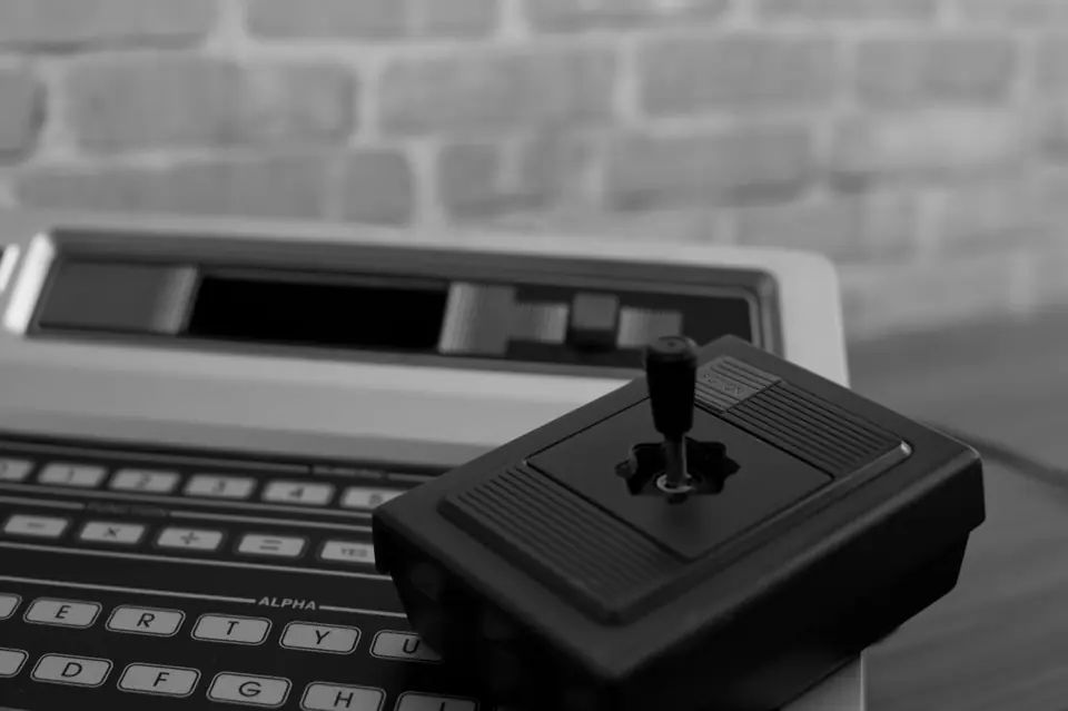A black joystick with a single stick sits on the keyboard of an old home computer.