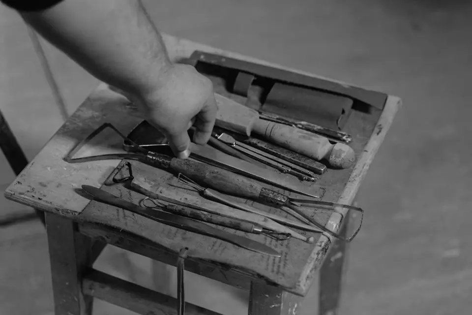 A hand arranges old screwdrivers, files and hand tools on a small paint-stained wooden stool.