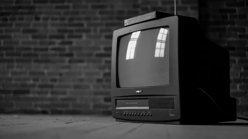 A small black tube television with a built-in tape player sits against a brick wall.
