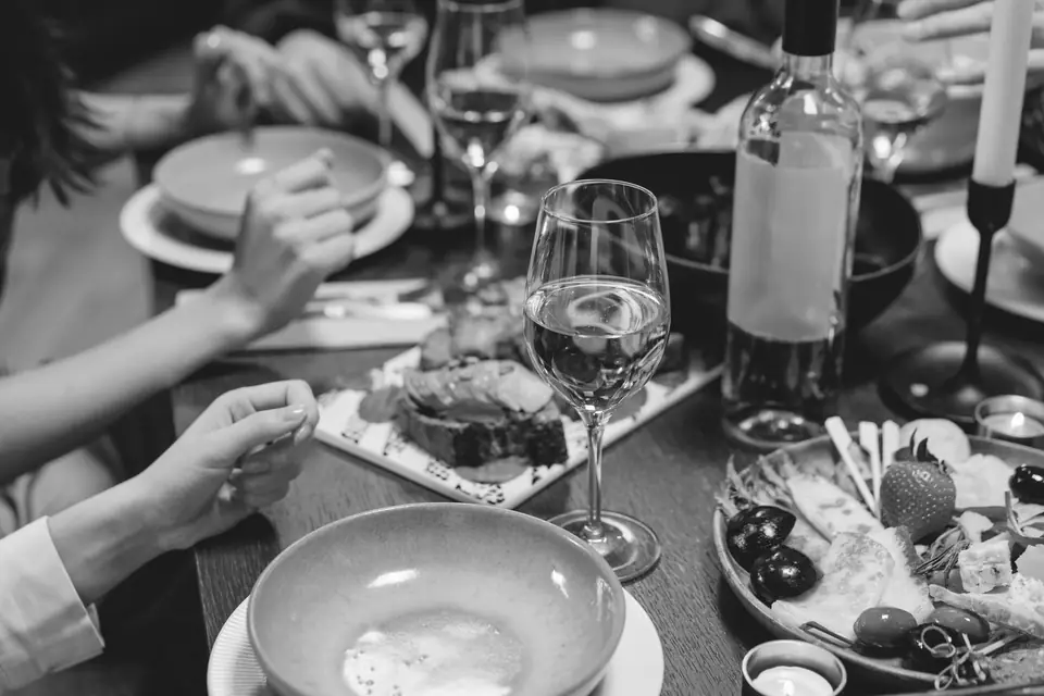 Several people share a dinner table set with wine glasses, a bottle, bowls and a platter of food.