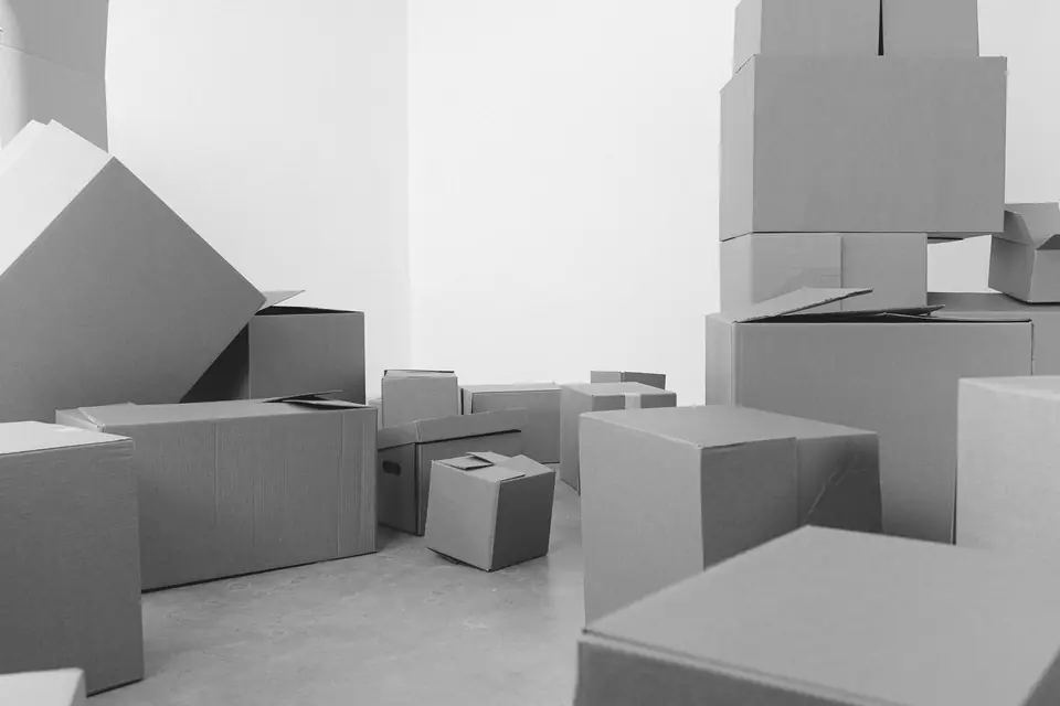 Many cardboard boxes of different sizes are stacked and scattered across a bare white room.