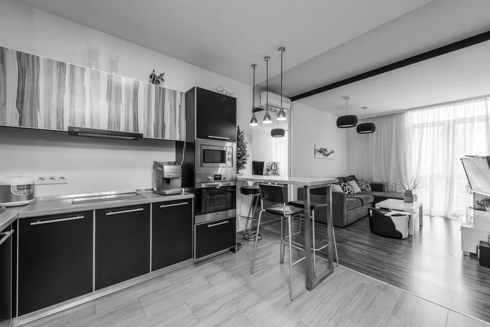An open-plan apartment has a modern kitchen with dark cabinets, a bar counter with stools and a sitting area.