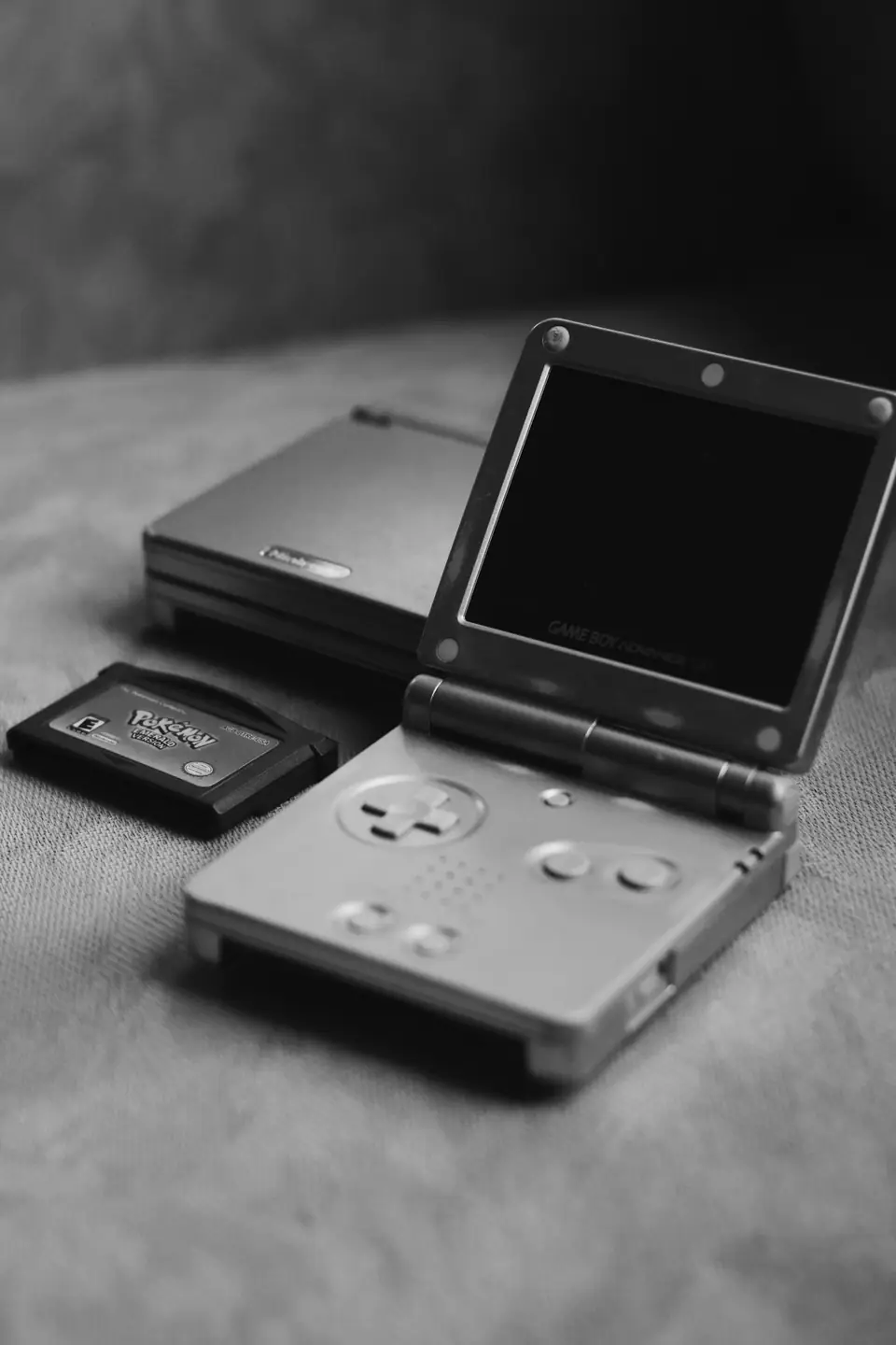 Two folding handheld game consoles sit on a table beside a small game cartridge.