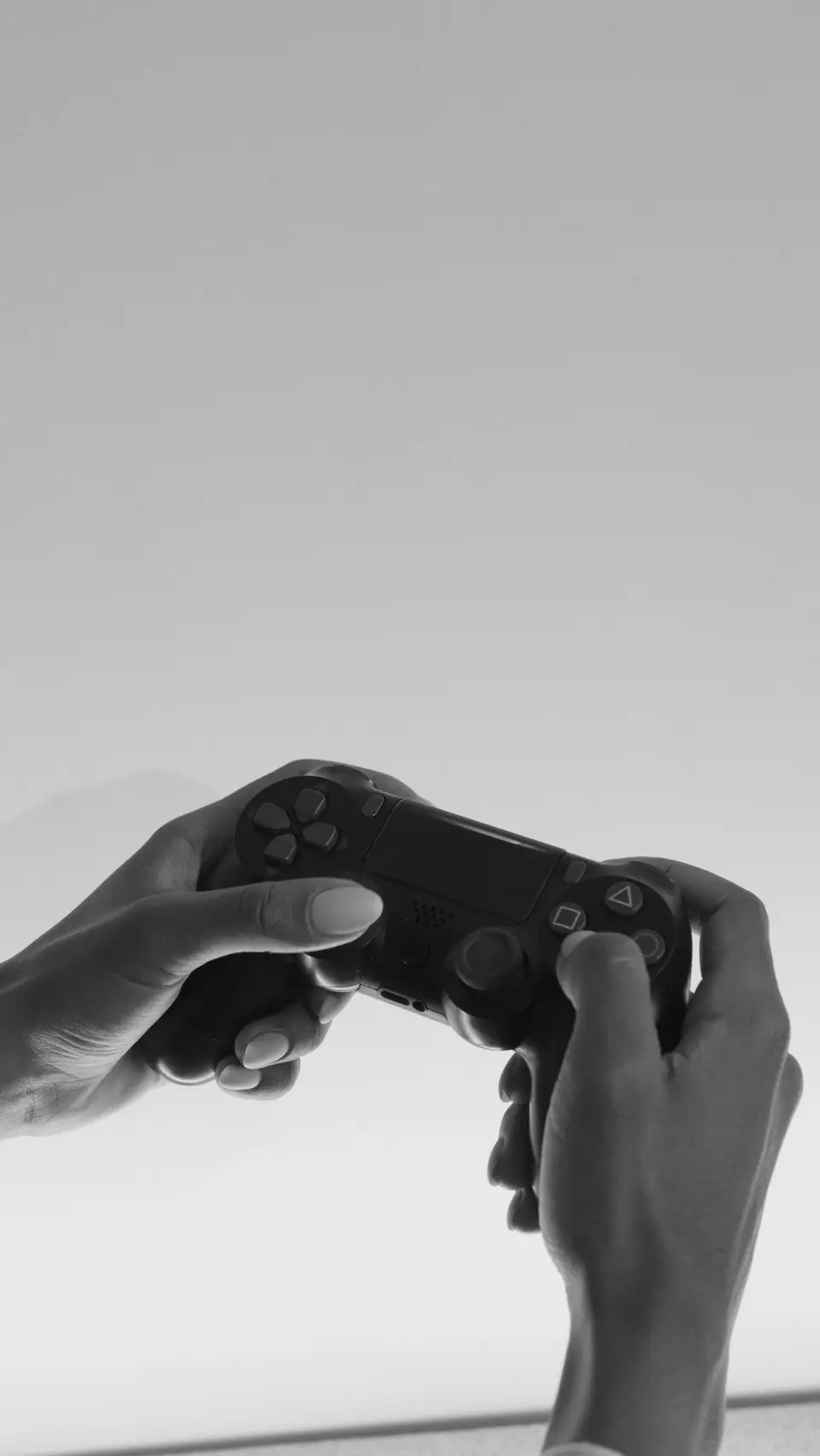 Two hands hold a black game controller up against a pale, empty sky.