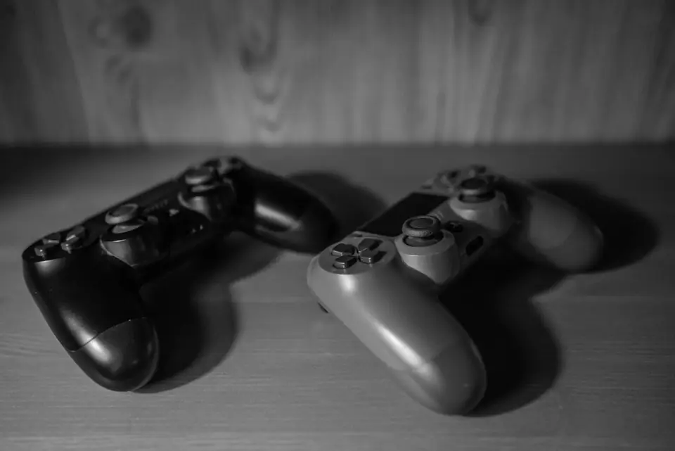 Two game controllers, one black and one light gray, rest on a wooden surface.