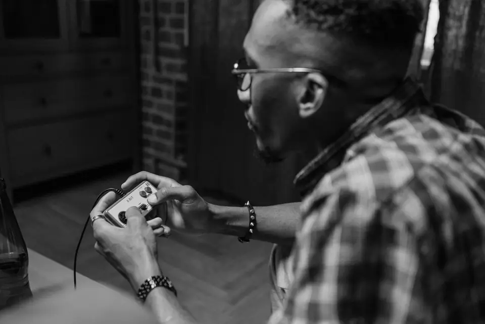 A man in glasses and a plaid shirt leans forward holding a game controller with both hands.