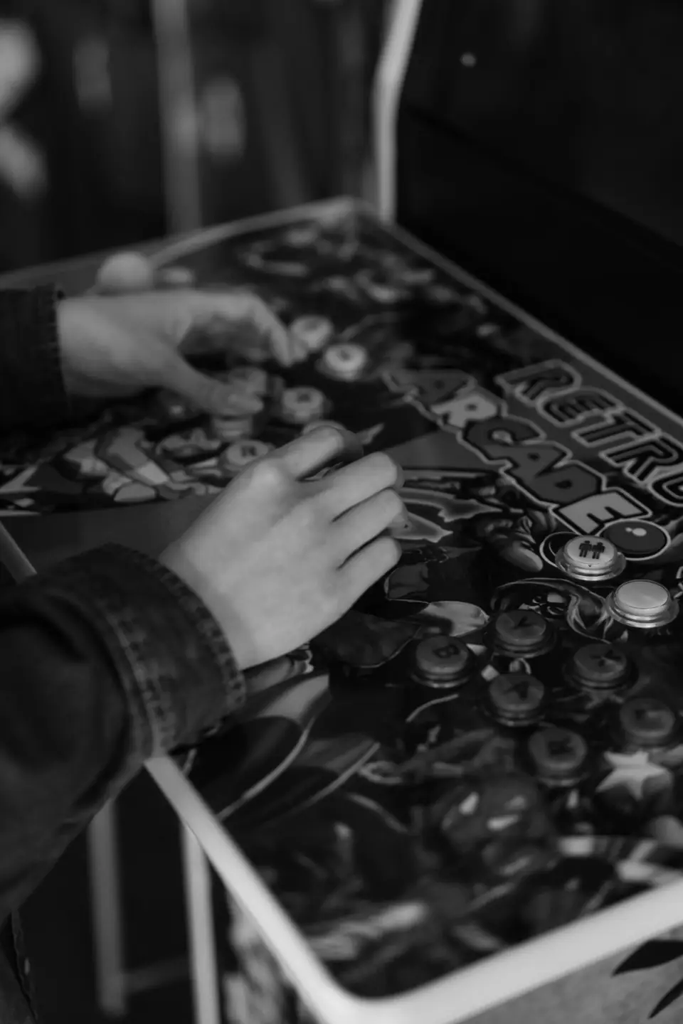 Two hands press buttons on a colorful arcade control panel with retro artwork.