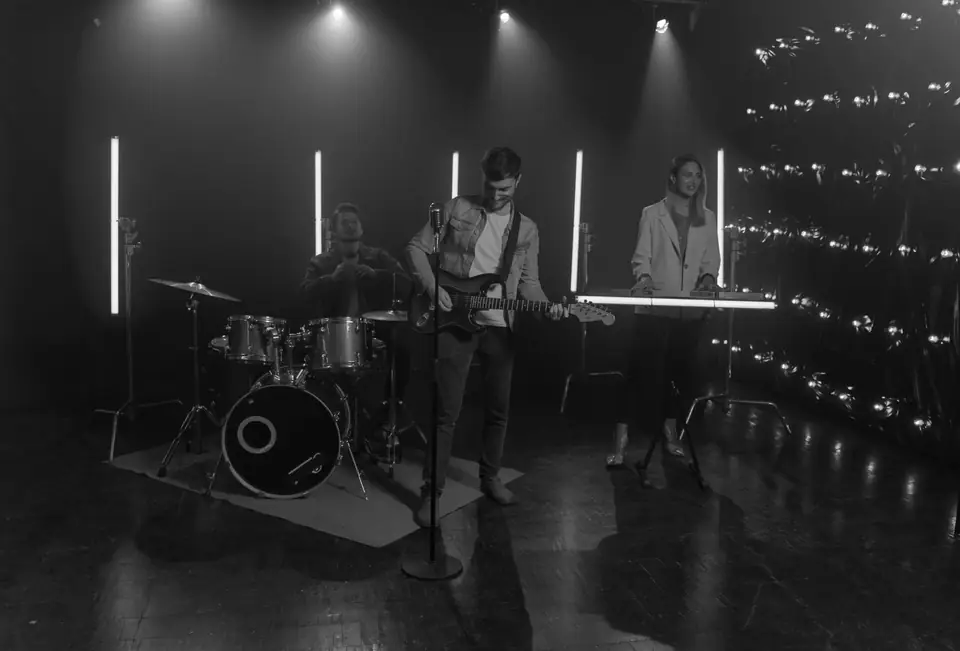 A band with drums, guitars and keyboard performs on a dark stage lit by vertical light tubes.