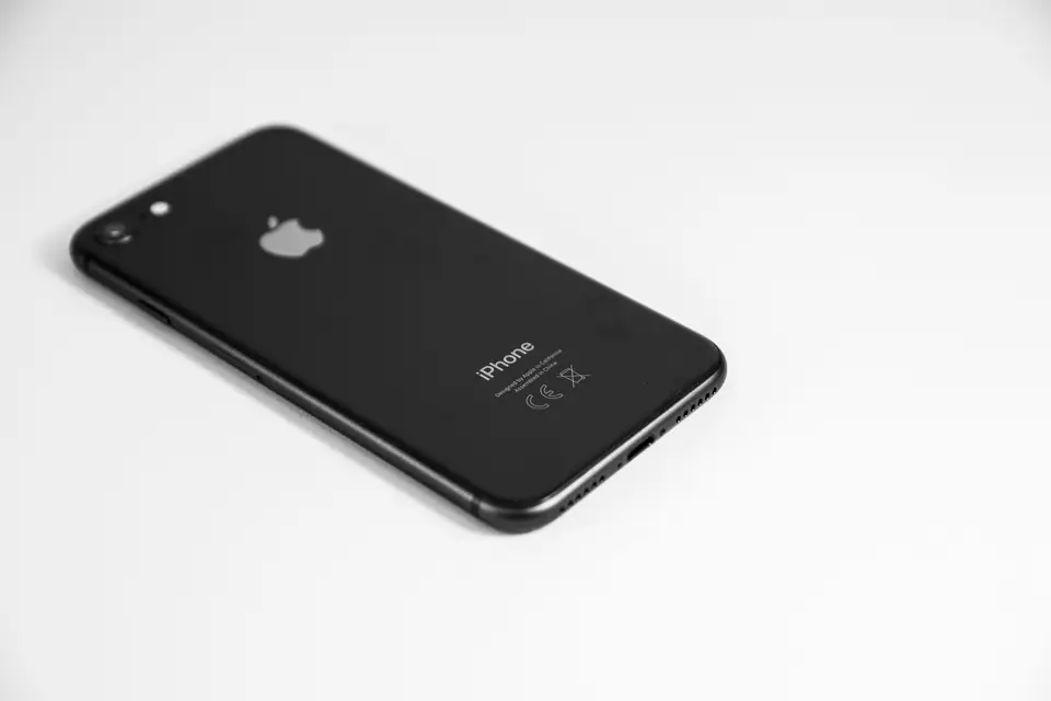 A black iPhone lies face down on a plain white surface, its rear camera and logo visible.