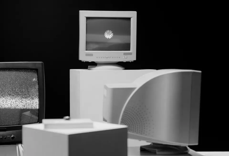 Several tube monitors and a television on white blocks sit in a dark room, one showing static.