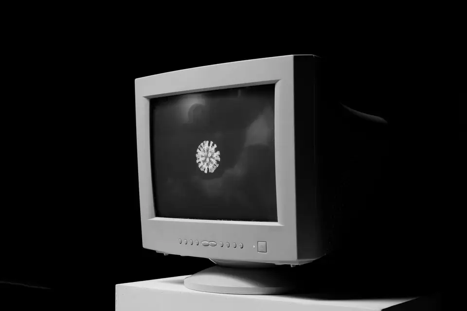 A beige tube computer monitor on a white plinth displays a small bright shape in darkness.