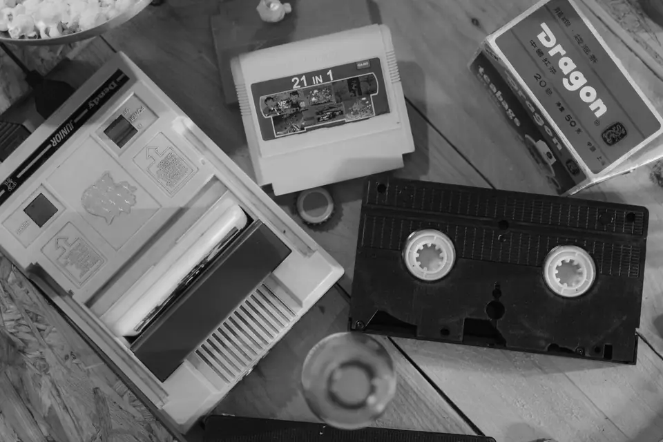 Game cartridges, a retro console and a videocassette lie scattered across a wooden table.